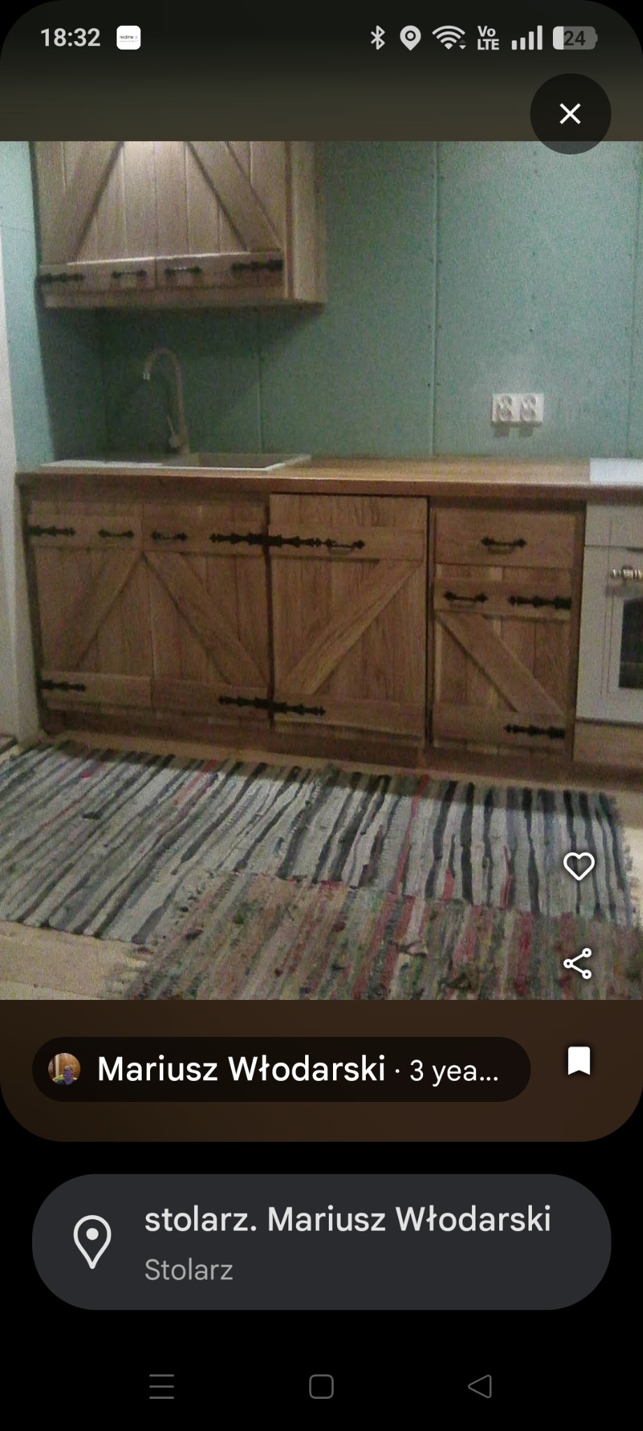 Rustykalna zabudowa kuchenna z drewnianymi frontami w stylu wiejskim, z czarnymi okuciami i dywanikiem w paski. Ujęcie z bliska, widoczny zlew i bateria.