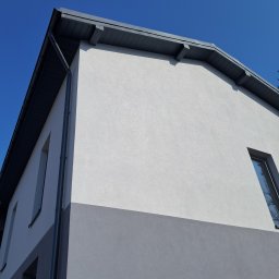 ŚWIST-BUD - Dwukolorowa elewacja domu w odcieniach szarości i bieli, z widocznymi oknami i rynnami, sfotografowana pod kątem w słoneczny dzień.