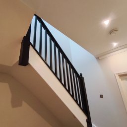 Prodecopainting - Schody po remoncie w Zarszynie: białe ściany, ciemna balustrada, widok z dołu. Nowoczesne wykończenie wnętrza, minimalistyczny design.