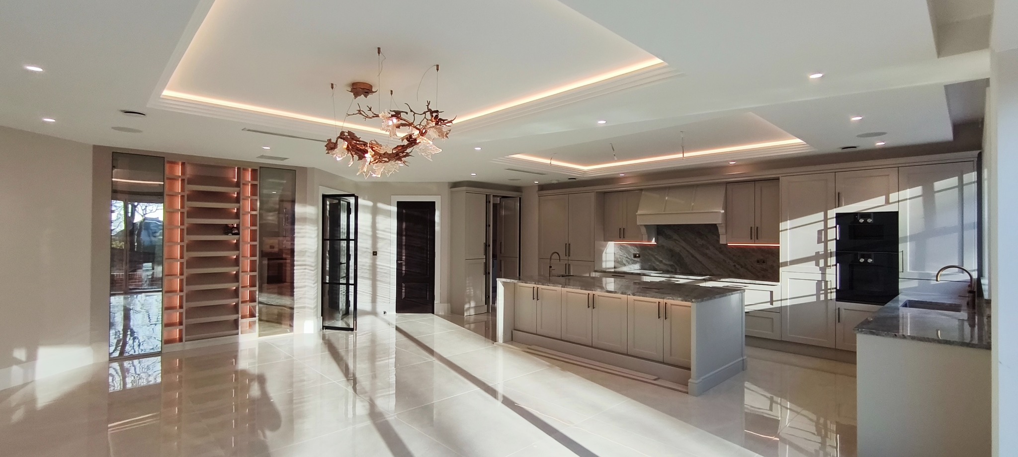 Eleganckie wykończenie wnętrza kuchni z wyspą, marmurowym blatem i designerską lampą. Jasne płytki podłogowe odbijają światło, podkreślając przestronność.