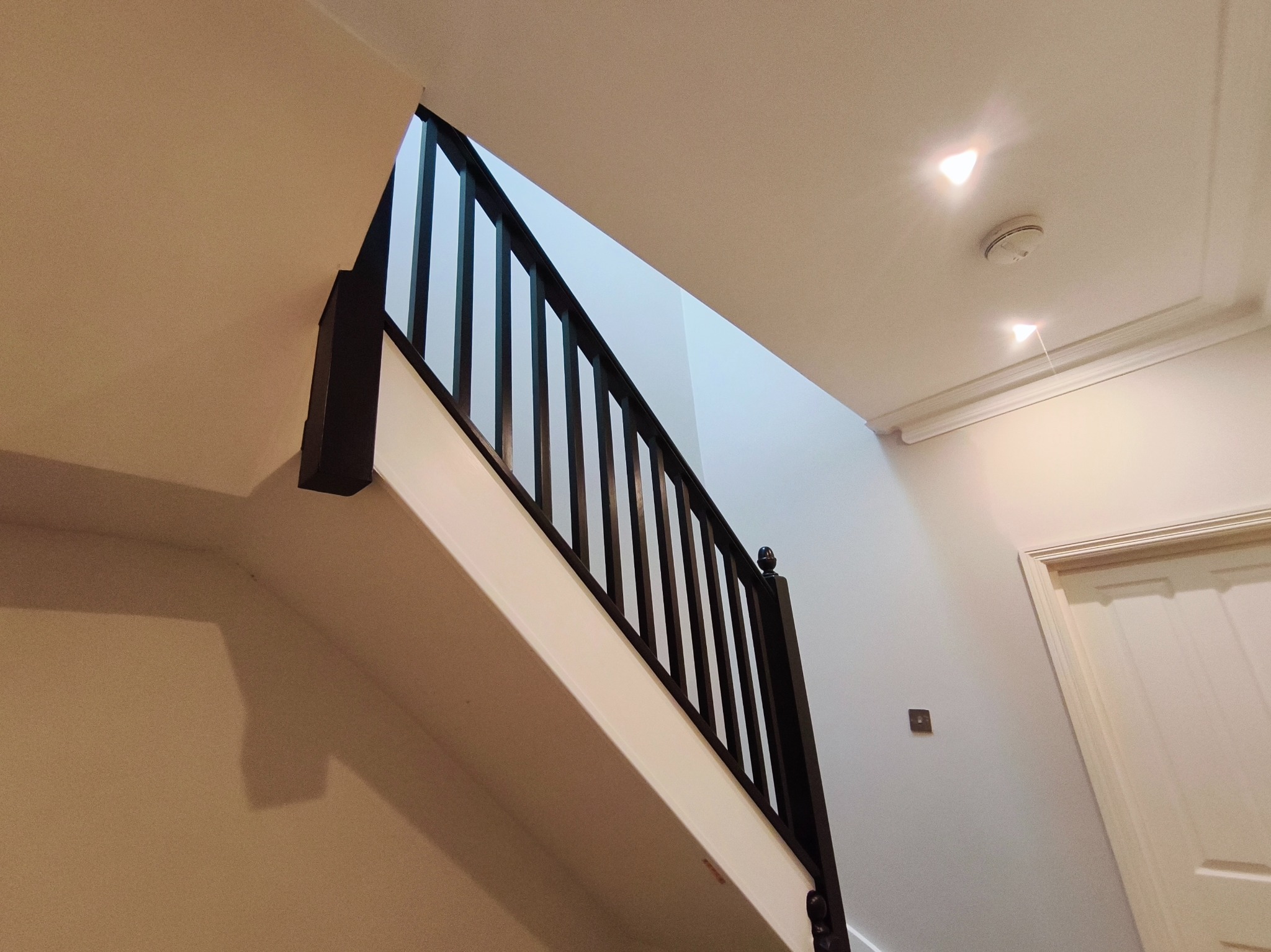 Schody po remoncie w Zarszynie: białe ściany, ciemna balustrada, widok z dołu. Nowoczesne wykończenie wnętrza, minimalistyczny design.