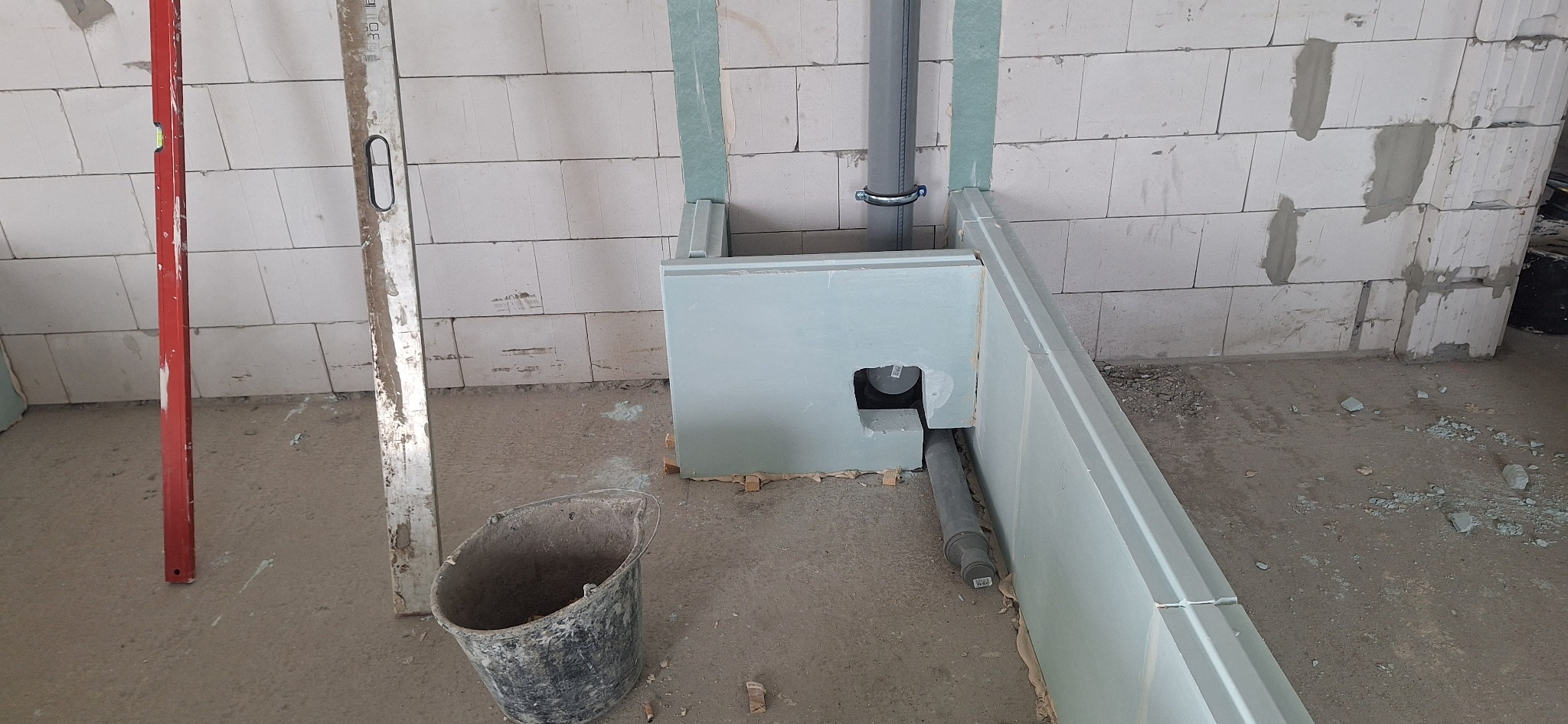 Niedokończona zabudowa z płyty gipsowej w surowym wnętrzu. Widoczne rury, poziomica i wiadro. Ściany z betonu komórkowego.
