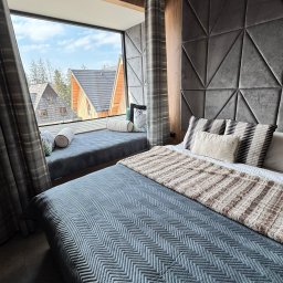 KARPIEL SHINE SERVICES SPÓŁKA Z OGRANICZONĄ ODPOWIEDZIALNOŚCIĄ - Stylowa sypialnia z dużym oknem i widokiem na góry. Szara tapicerowana ściana z geometrycznym wzorem. Na parapecie poduszki dekoracyjne.