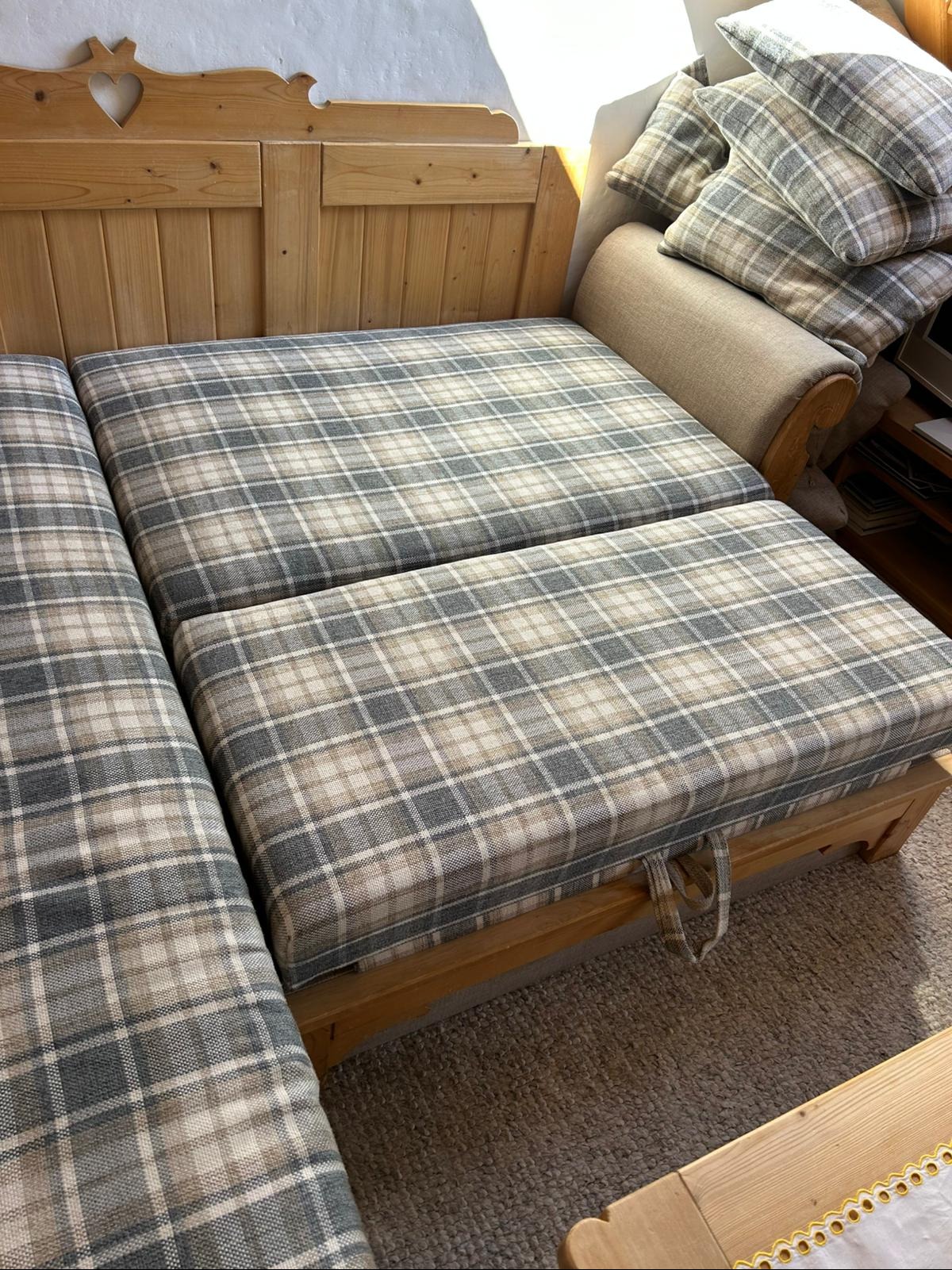 Drewniana sofa z poduszkami w kratę, widoczne detale wykończenia i tekstylna faktura. Jasne, naturalne światło podkreśla ciepłą kolorystykę mebla.