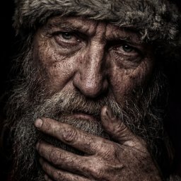 Umbralux - Portret zmęczonego mężczyzny z brodą w czapce Mikołaja, z głębokimi zmarszczkami i dłonią przy twarzy, w ciemnym otoczeniu. Wyraziste detale skóry i faktury.