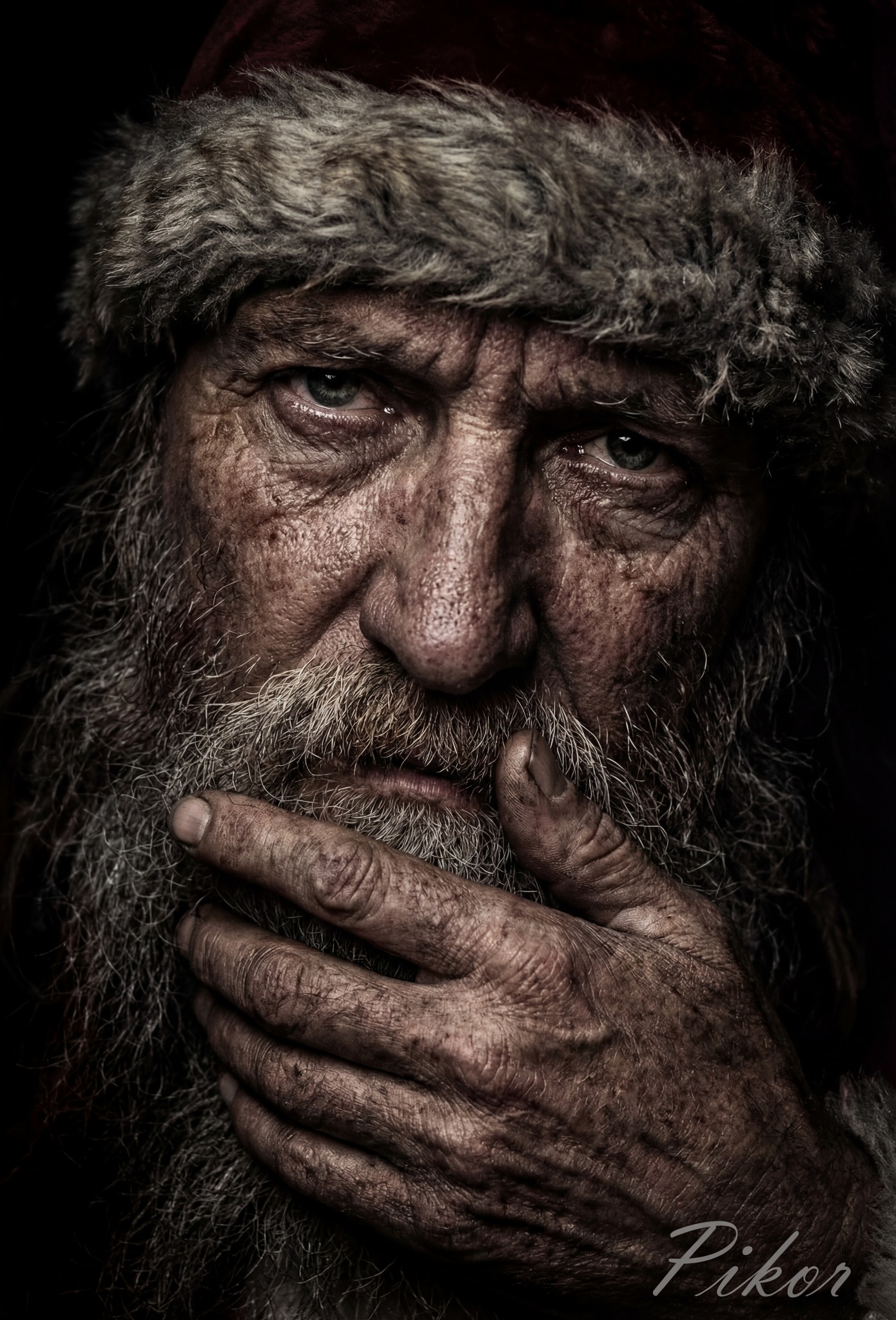 Portret zmęczonego mężczyzny z brodą w czapce Mikołaja, z głębokimi zmarszczkami i dłonią przy twarzy, w ciemnym otoczeniu. Wyraziste detale skóry i faktury.