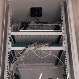 Filip Smoleń - Szafa rack z zamontowanym rejestratorem monitoringu Hikvision, okablowaniem i listwą zasilającą. Widoczne przewody i elementy instalacji.
