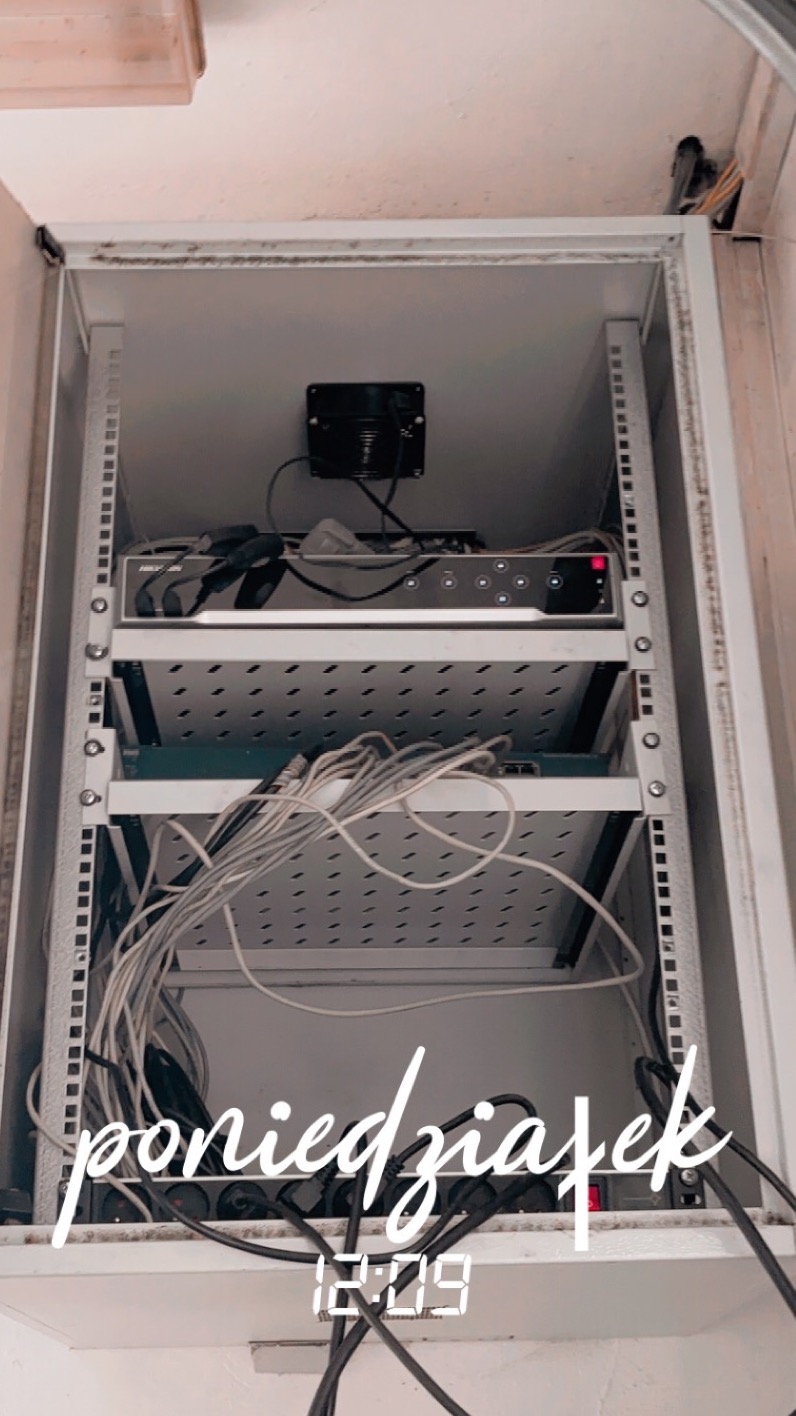 Szafa rack z zamontowanym rejestratorem monitoringu Hikvision, okablowaniem i listwą zasilającą. Widoczne przewody i elementy instalacji.