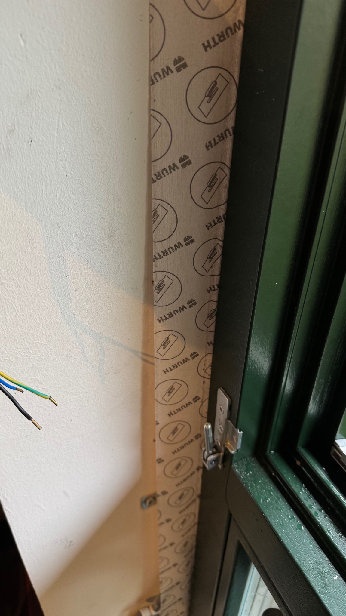 Montaż okna: widok na uszczelnienie ramy okiennej z użyciem taśmy Wurth, z widocznymi przewodami elektrycznymi w ścianie. Detal montażowy.