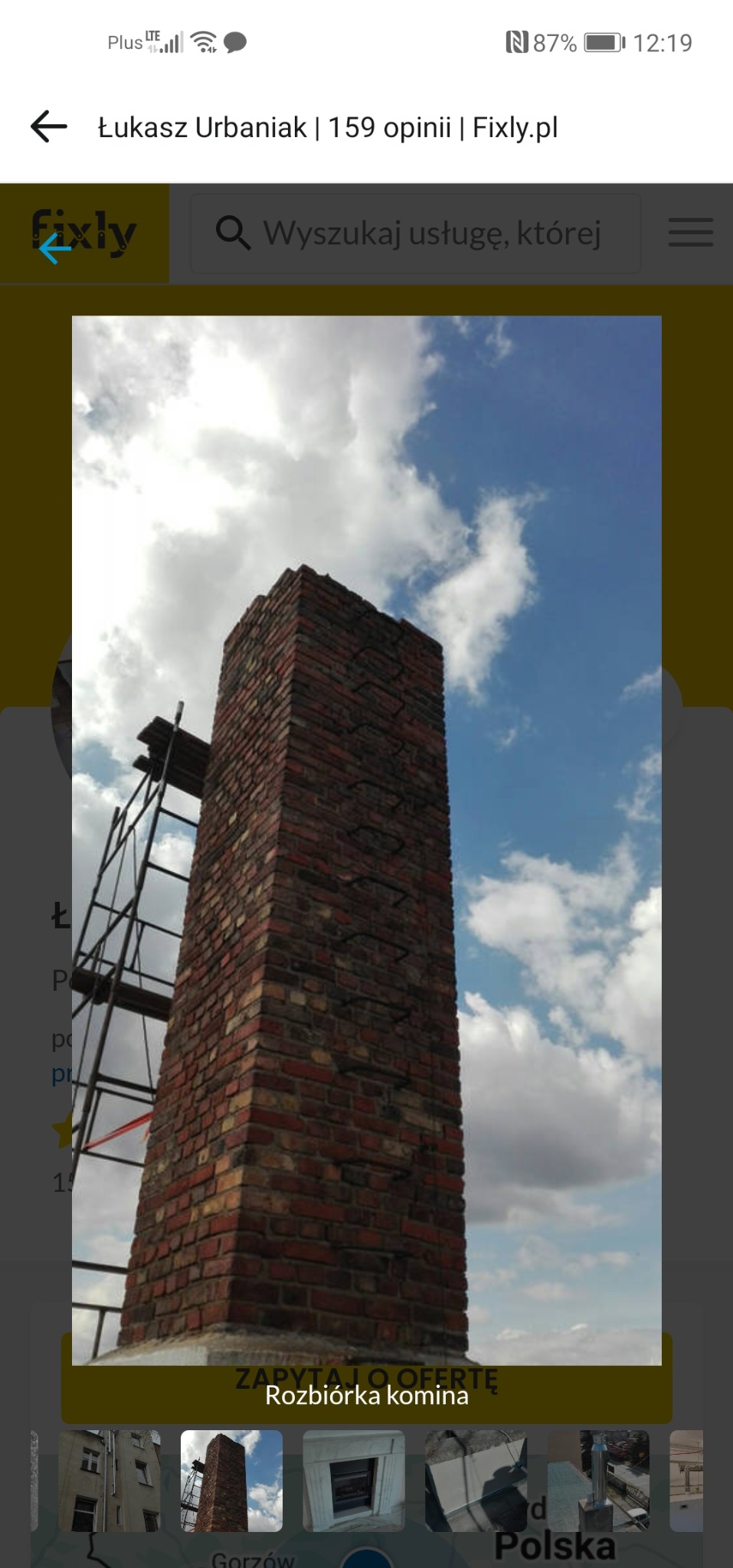 Wysoki, ceglany komin z metalową konstrukcją rusztowania na tle błękitnego nieba z chmurami. Widok z dołu, podkreślający wysokość komina.