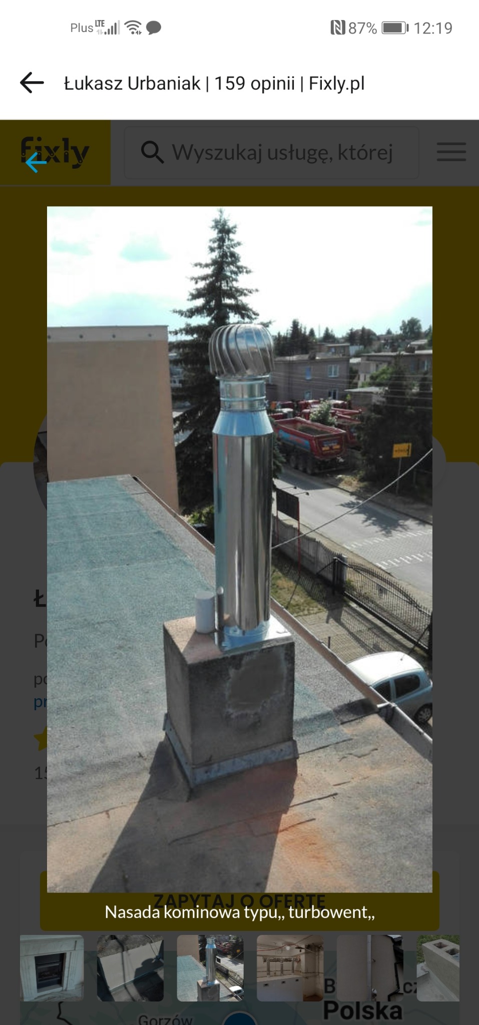 Turbowent na kominie z betonową podstawą, widok z góry na dach budynku i otoczenie. Stalowa konstrukcja na tle zieleni i zabudowań.