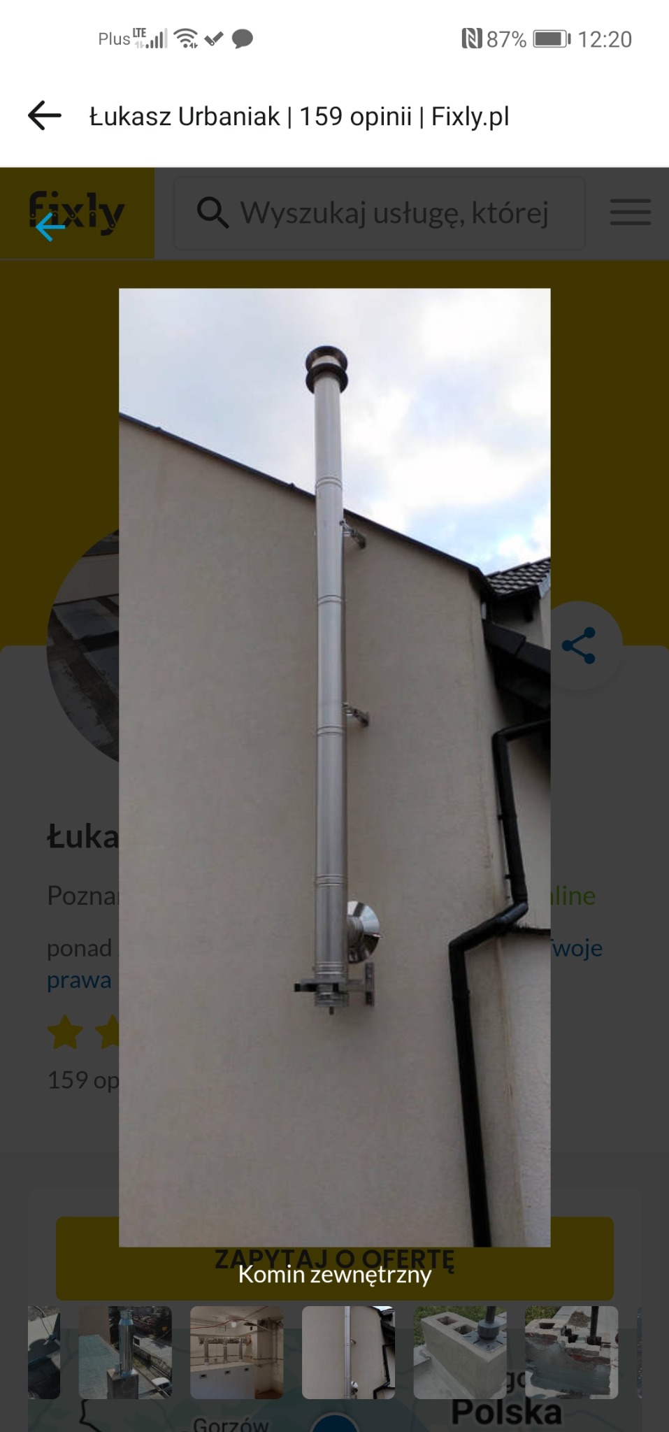 Zewnętrzny, stalowy komin systemowy zamontowany na ścianie budynku. Widoczne elementy mocujące i fragment dachu. Ujęcie z dołu, pochmurne niebo w tle.