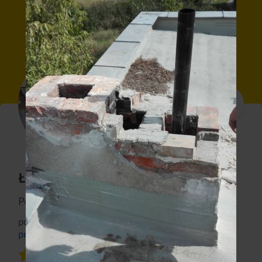 Ceglany komin na dachu po naprawie, z widocznymi śladami cementu i nową rurą. Tło stanowi zieleń drzew i krzewów.