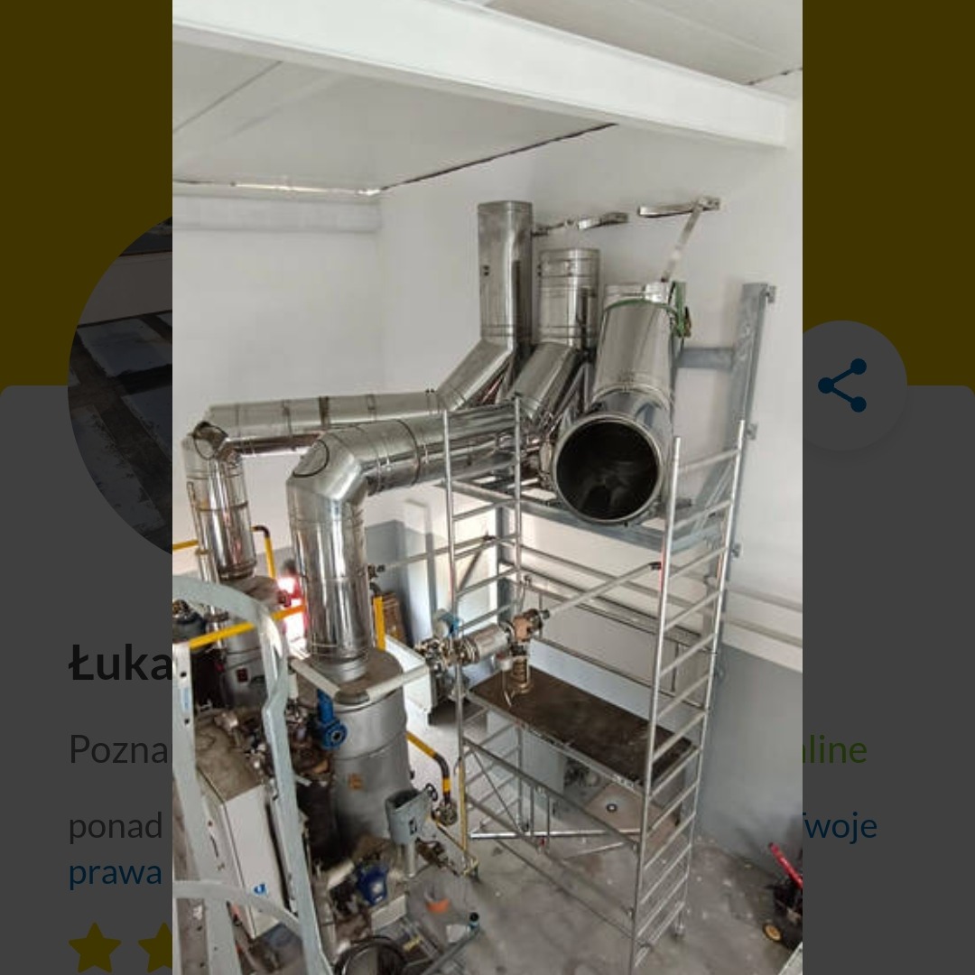 Skomplikowany system rur ze stali nierdzewnej, prawdopodobnie wentylacyjnych, zamontowany w pomieszczeniu przemysłowym, widoczny rusztowanie.