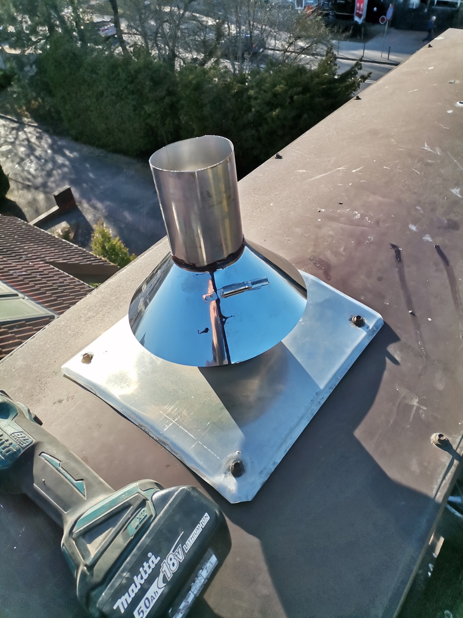 Metalowy wkład kominowy z narzędziem w tle, widok z góry. Usługa wykonana w Poznaniu. Błyszcząca powierzchnia odbija otoczenie.