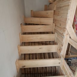 Schody betonowe Fran-Bud - Szczegółowe ujęcie drewnianego szalunku schodów betonowych z widocznym zbrojeniem, w trakcie budowy. Widoczne narzędzia i elementy konstrukcyjne.