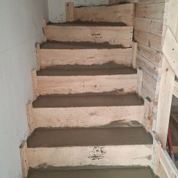 Schody betonowe Fran-Bud - Wnętrze z drewnianym szalunkiem schodów wypełnionym świeżym betonem, ukazujące etap budowy. Widoczne deski szalunkowe i surowy beton na stopniach.