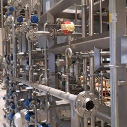 Weldingteam - Kompleksowa instalacja przemysłowa z rur ze stali nierdzewnej, z licznymi zaworami i elementami łączeniowymi, w hali produkcyjnej.