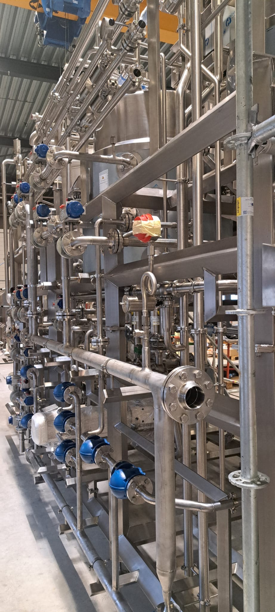 Kompleksowa instalacja przemysłowa z rur ze stali nierdzewnej, z licznymi zaworami i elementami łączeniowymi, w hali produkcyjnej.