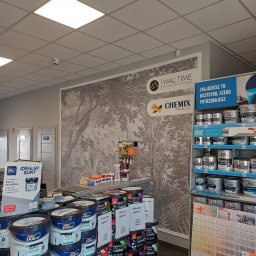 Chemix Oława Sp. z o.o. - Sklep z farbami i tapetami: ściana z tapetą w leśny motyw, regały z farbami Dulux i Tikkurila, ekspozycja kolorów. Widoczne logo Walltime i Chemix.