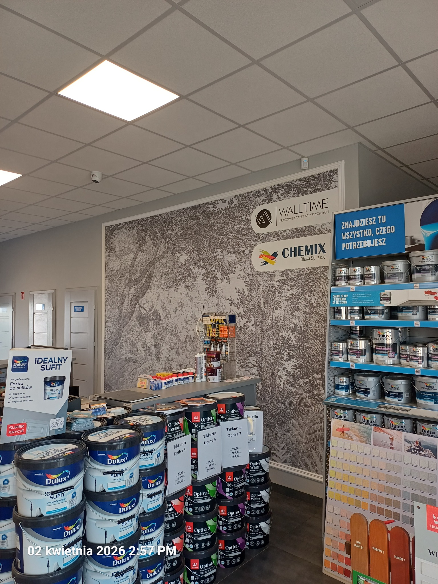 Sklep z farbami i tapetami: ściana z tapetą w leśny motyw, regały z farbami Dulux i Tikkurila, ekspozycja kolorów. Widoczne logo Walltime i Chemix.