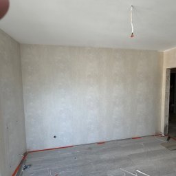 Vitalii Usenko - Pokój po malowaniu ścian na beżowo z delikatnym wzorem. Podłoga zabezpieczona folią malarską. Widoczne gniazdko elektryczne i wystające kable z sufitu.