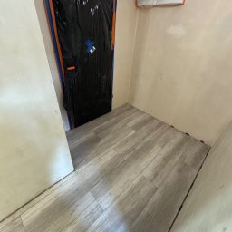 Vitalii Usenko - Przygotowane do malowania pomieszczenie z zabezpieczonymi drzwiami folią i nową podłogą. Widoczna skrzynka elektryczna na ścianie.