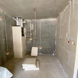 FixHouse Grzegorz Rzepa - Surowy stan łazienki w trakcie remontu: widoczne płyty karton-gips na ścianach, instalacja elektryczna i wentylacyjna, przygotowane płytki na podłodze.