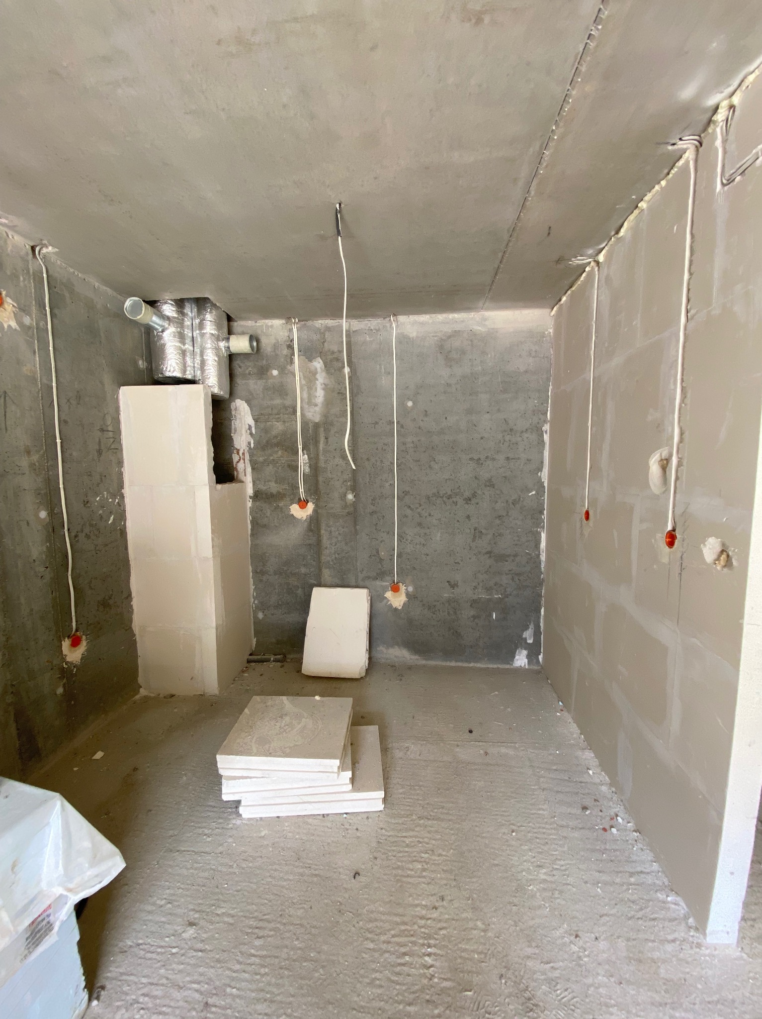 Surowy stan łazienki w trakcie remontu: widoczne płyty karton-gips na ścianach, instalacja elektryczna i wentylacyjna, przygotowane płytki na podłodze.