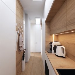 Interiors by Marlena - Nowoczesny przedpokój z zabudową meblową: białe szafy, drewniane panele, wieszaki na ubrania, oświetlenie LED, ekspres do kawy. Minimalistyczny design, ciepłe oświetlenie.