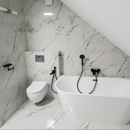 SENDO - Biała, wolnostojąca wanna i toaleta w nowoczesnej łazience z marmurowymi płytkami. Czarna armatura i akcesoria. Poddasze ze skosem.