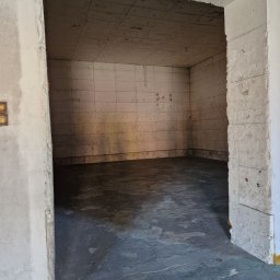 Wynajem chłodni - Wnętrze chłodni z betonowymi ścianami i podłogą, widoczne ślady wilgoci. Otwór wejściowy z surowym wykończeniem. Sufit z paneli. Widok z zewnątrz.