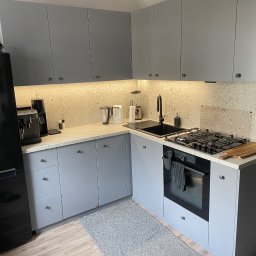 The Wood Life - Szara zabudowa kuchenna z blatem Terrazzo K095 SU i sprzętem AGD w Papowo Toruńskie. Fronty lakierowane mat RAL 7004, zawiasy Blum, szuflady HAFELE.