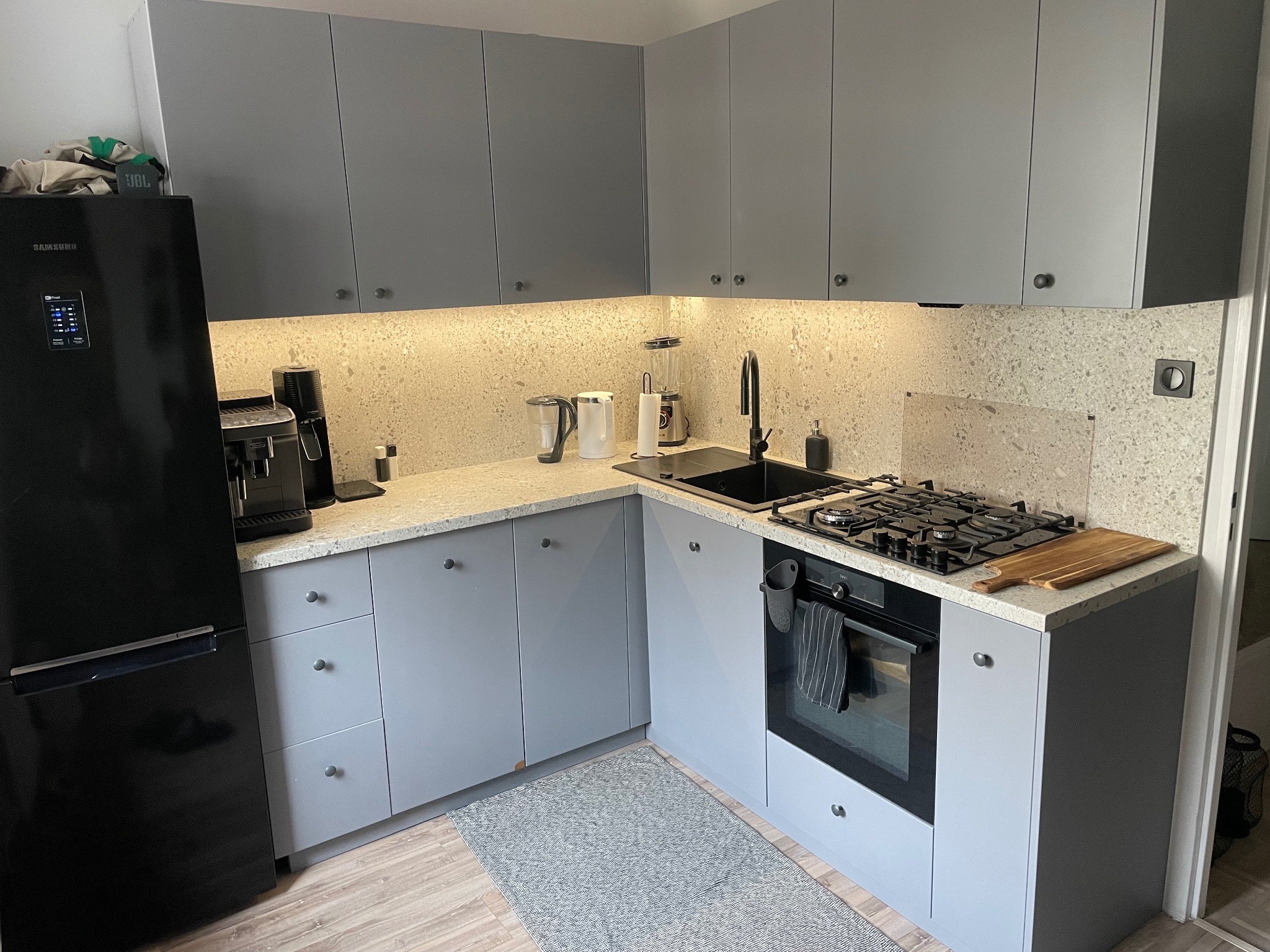 Szara zabudowa kuchenna z blatem Terrazzo K095 SU i sprzętem AGD w Papowo Toruńskie. Fronty lakierowane mat RAL 7004, zawiasy Blum, szuflady HAFELE.