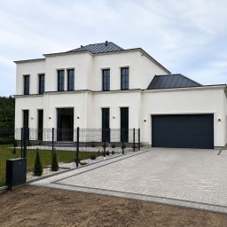 Fillpro Ivan Filiarovskyi - Elegancki dom jednorodzinny z jasną elewacją, ciemną stolarką okienną i grafitowym dachem. Nowoczesne wykończenie z kostki brukowej i minimalistycznym ogrodzeniem.