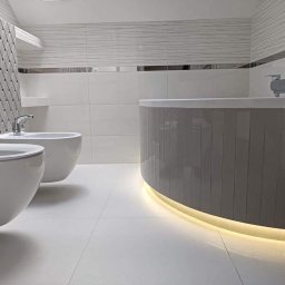 Czad Bud Kinga Sadowa - Nowoczesna łazienka w bieli i szarości z podświetlaną wanną, umywalką i bidetem. Geometryczne płytki na ścianie dodają unikalnego charakteru.