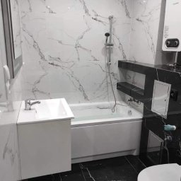 Czad Bud Kinga Sadowa - Wykończona łazienka z wanną, umywalką i toaletą. Białe marmurowe płytki na ścianach kontrastują z czarną marmurową podłogą. Nowoczesny design, oświetlenie punktowe.