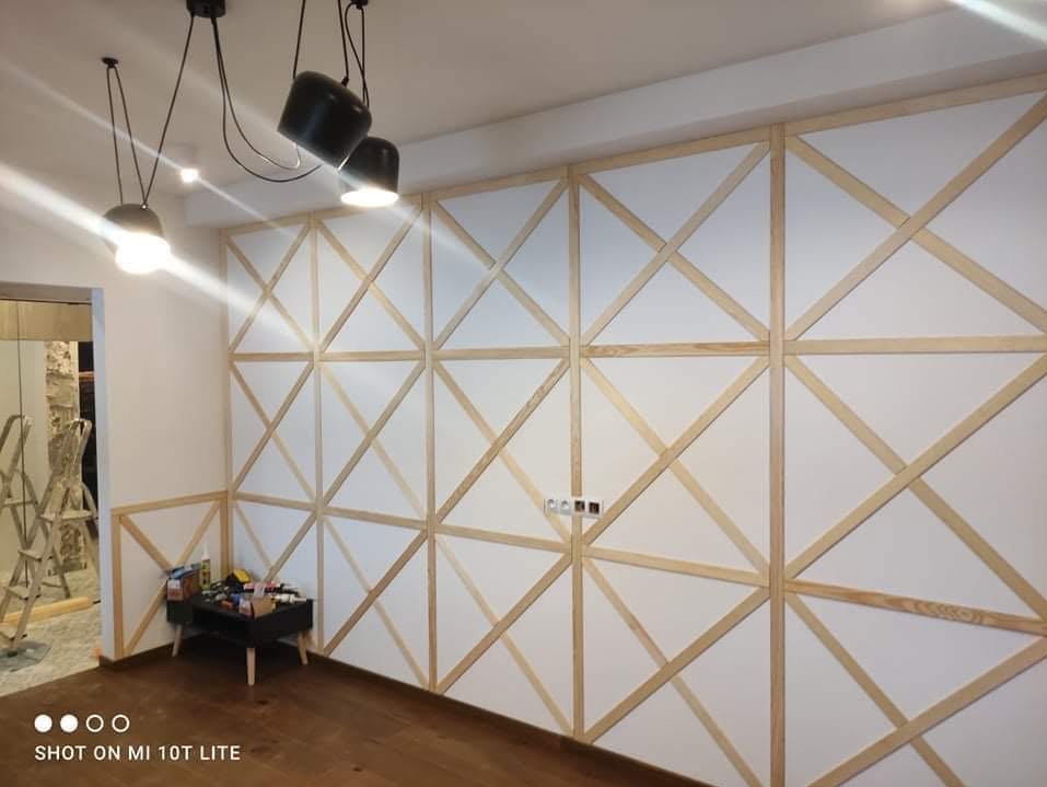 Ściana z dekoracyjną, drewnianą kratownicą w jasnym wnętrzu. Widoczne minimalistyczne lampy sufitowe i drewniana podłoga. Element wykończenia wnętrza.