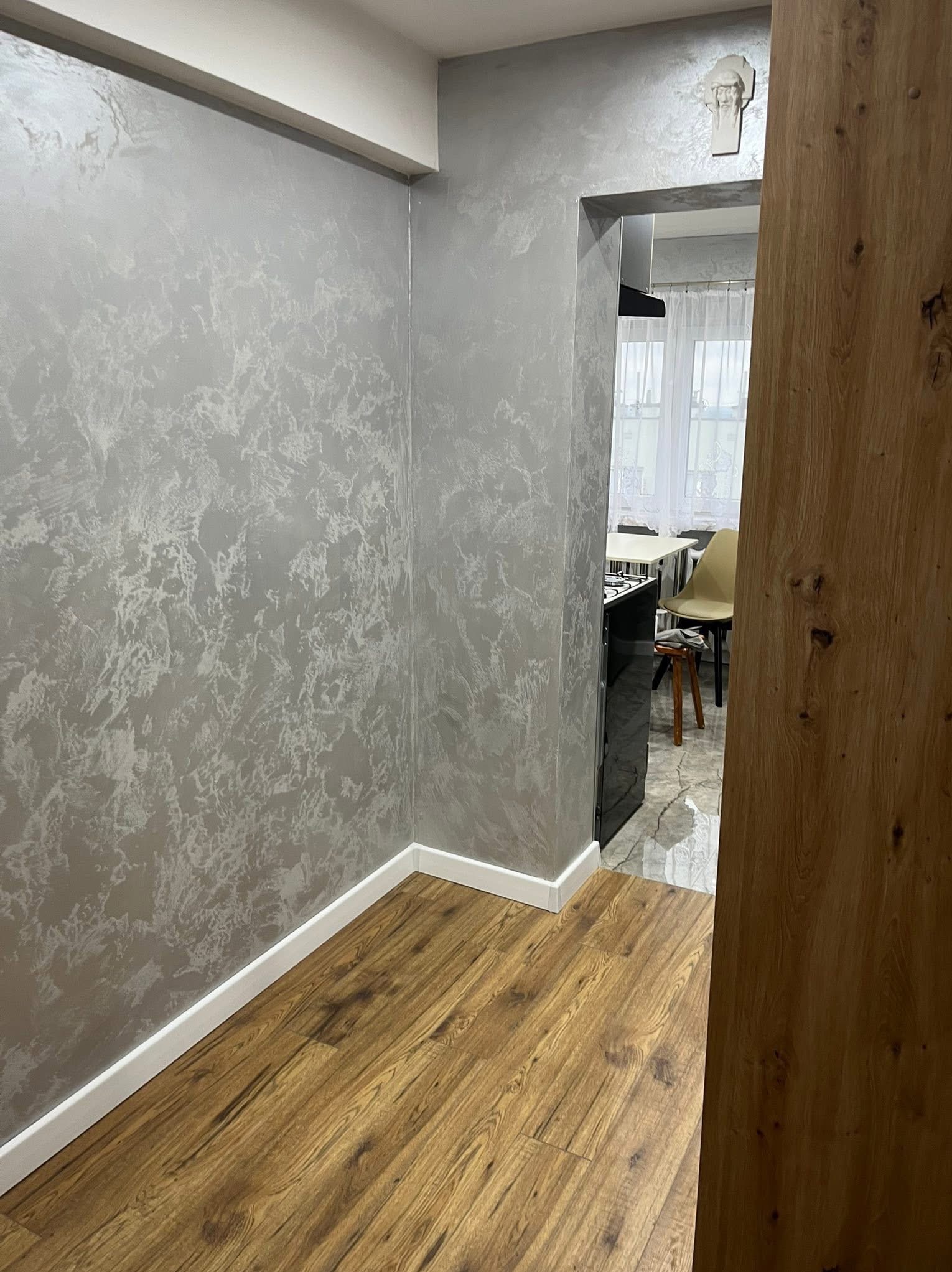 Korytarz po malowaniu dekoracyjnym ścian na srebrno z efektem marmuru, widoczna drewniana podłoga i fragment kuchni w tle. Dekoracja nad przejściem.