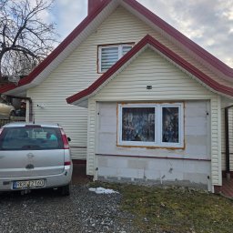 Audyty energetyczne. House Energy. Katarzyna Fejkiel - Dom z sidingiem i nowym oknem w trakcie montażu, widoczna piana montażowa. Na podjeździe stoi srebrny samochód osobowy. Pochmurne niebo w tle.