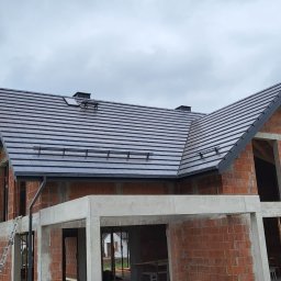 F.H.U TOMBUD - Dom w trakcie budowy z ciemnoszarym, nowym dachem z dachówki ceramicznej. Widoczne kominki wentylacyjne i drabinki przeciwśniegowe. Surowy stan budynku.