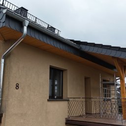 F.H.U TOMBUD - Dom z nowym, grafitowym dachem łupkowym i orynnowaniem. Widoczny fragment balkonu z drewnianą konstrukcją. Na ścianie numer domu '8'.