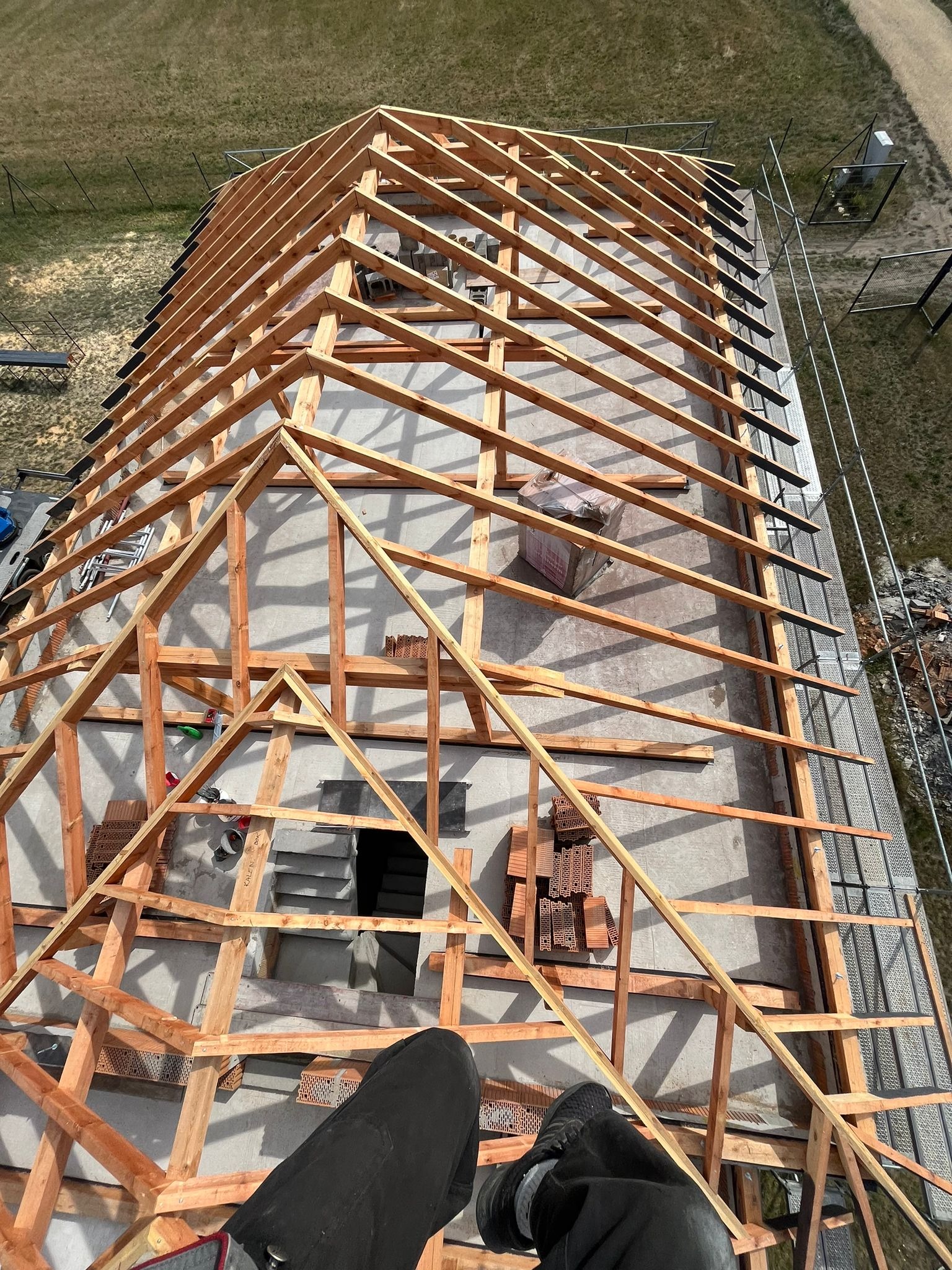 Wznoszenie drewnianej konstrukcji dachu z perspektywy lotu ptaka w Kalinowie. Widoczna więźba dachowa, elementy deskowania i przygotowane materiały do krycia.