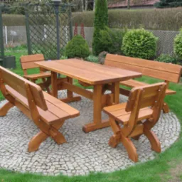 Drewniany zestaw mebli ogrodowych: stół i ławki z oparciami, ustawione na kamiennym bruku w ogrodzie. Widoczne krzewy i trawnik w tle.