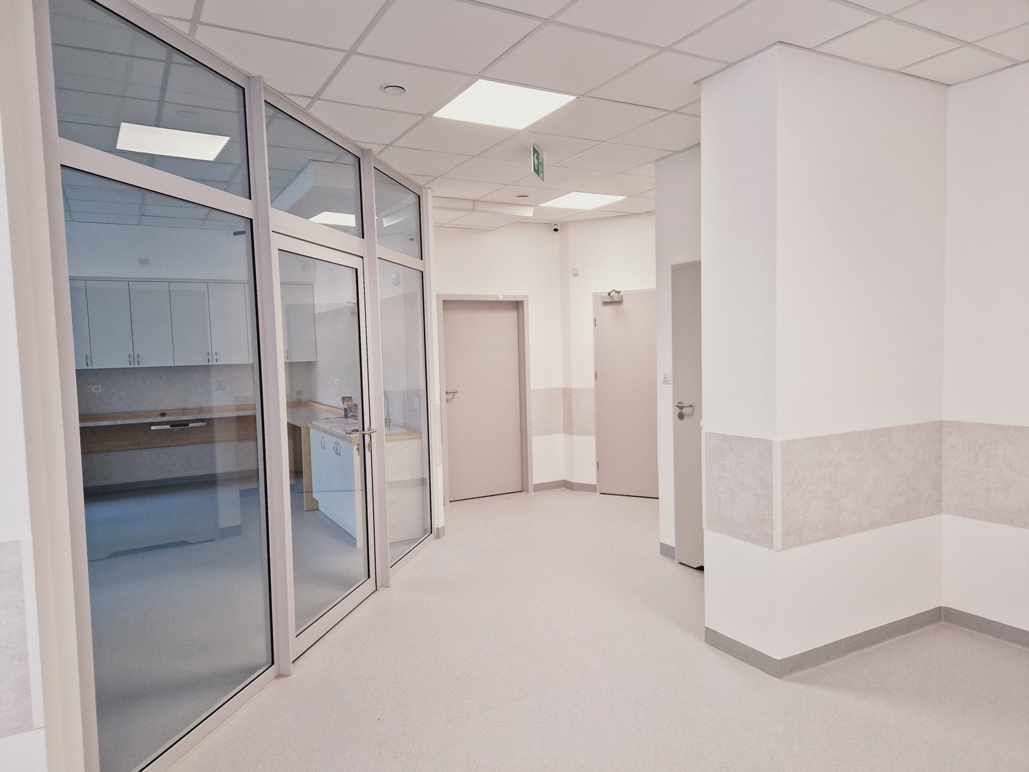 Jasne, przestronne wnętrze z przeszkloną ścianą działową, widok na pomieszczenie z zabudową kuchenną. Minimalistyczny design, neutralna kolorystyka, gładkie powierzchnie.