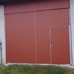 Sławomir - Ciemnobrązowa brama garażowa segmentowa z drzwiami wejściowymi, obok ściana z białej cegły i trawa. Widok z dołu, oświetlenie dzienne.