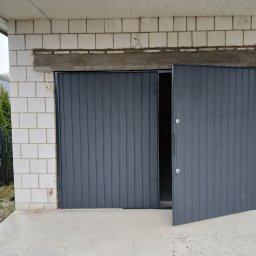 Sławomir - Szara brama garażowa segmentowa, częściowo otwarta, z widocznym zamkiem, zamontowana w surowym murze z białych bloczków betonowych. Widok z zewnątrz.