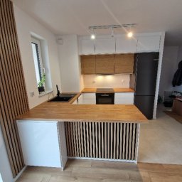 grzegorz skarzynski - Nowoczesna kuchnia z drewnianym blatem i lamelami. Białe szafki górne i dolne, czarny zlew i sprzęt AGD. Jasna podłoga i oświetlenie punktowe.