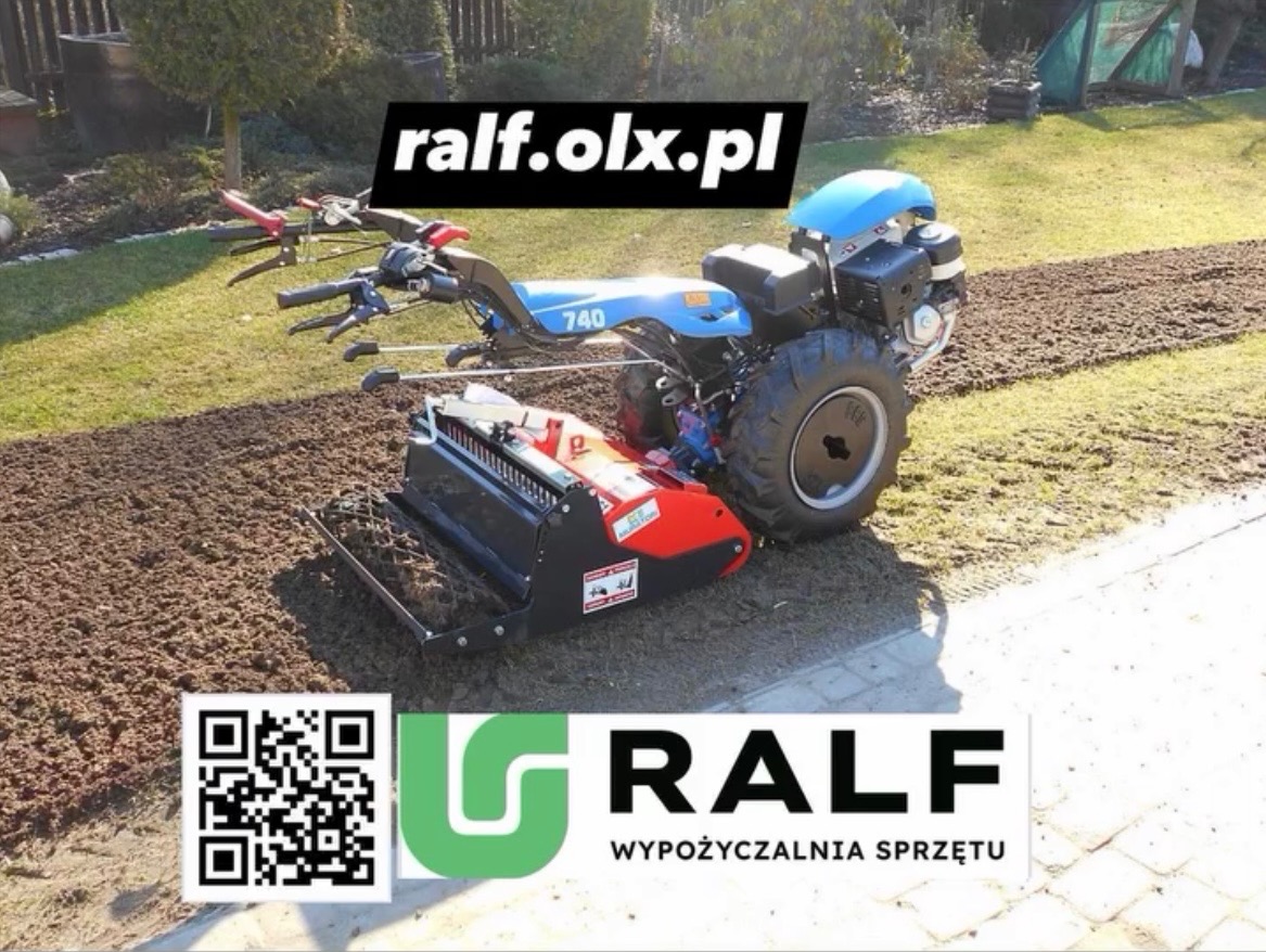 Niebieski glebogryz z czerwonym elementem roboczym na trawniku z przygotowaną glebą. Widoczne ślady pracy maszyny.