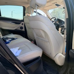 Auto Spa - Wnętrze samochodu z jasną, zabrudzoną tapicerką skórzaną na tylnych siedzeniach. Widoczne ślady użytkowania i zabrudzenia na oparciu fotela. Na siedzeniu leżą dokumenty i bluza.